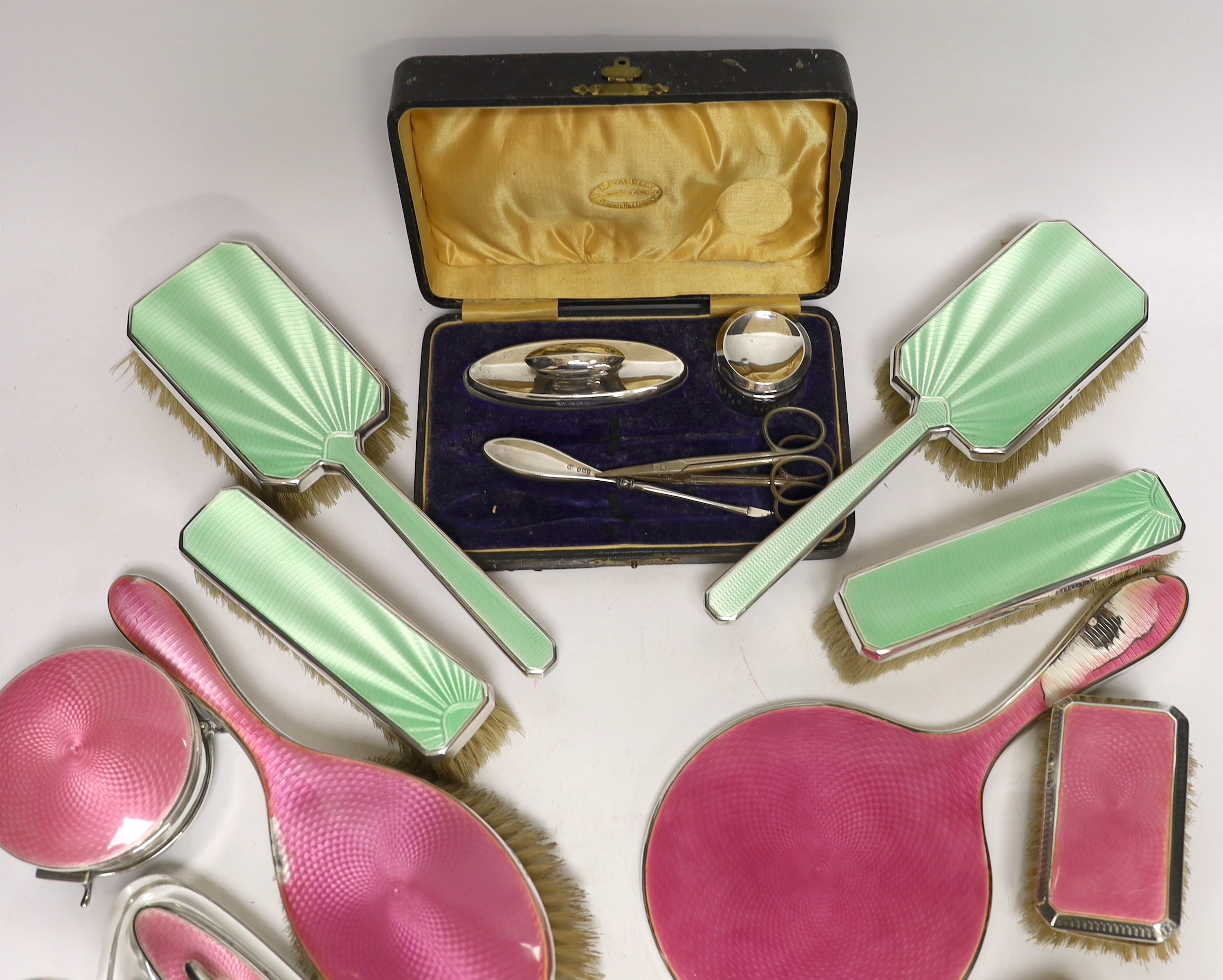 A 1930's five piece silver and green enamel mounted mirror and brush set by Mappin & Webb, a 1920's six piece silver and pink enamel mirror and brush set and two part manicure sets.